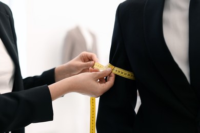 Photo of Tailor measuring jacket on man in atelier, closeup
