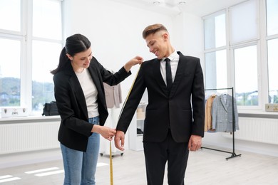 Photo of Tailor measuring jacket on man in atelier