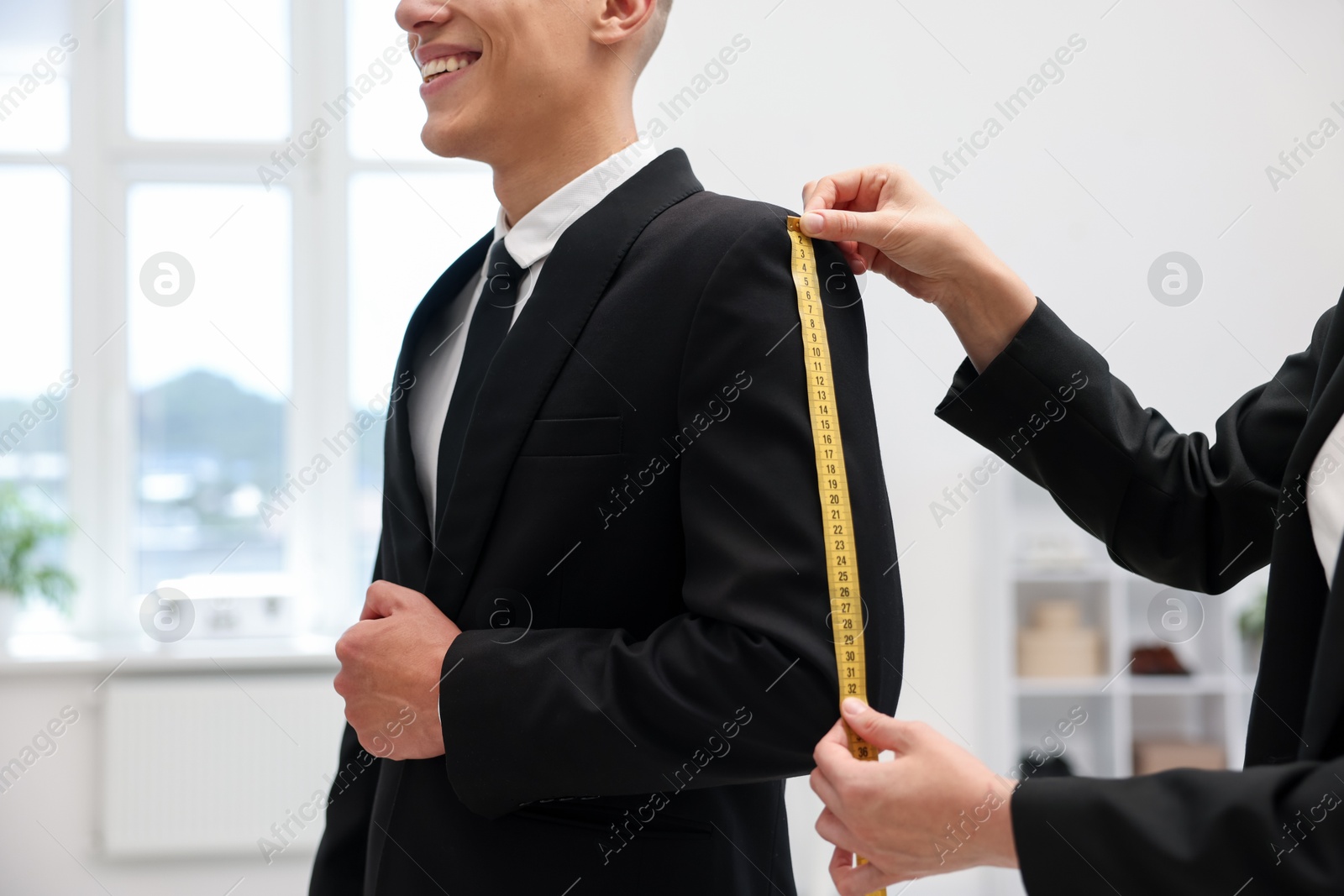 Photo of Tailor measuring jacket on man in atelier, closeup