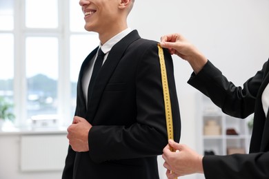 Photo of Tailor measuring jacket on man in atelier, closeup