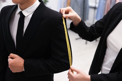 Photo of Tailor measuring jacket on man in atelier, closeup