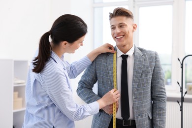 Photo of Tailor measuring jacket on man in atelier
