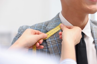 Photo of Tailor measuring jacket on man in atelier, closeup