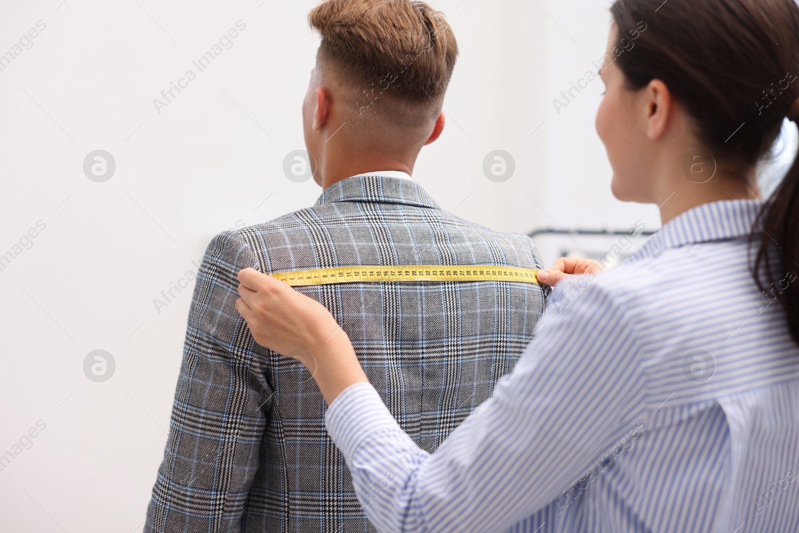 Photo of Tailor measuring jacket on man in atelier, back view