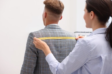 Photo of Tailor measuring jacket on man in atelier, back view