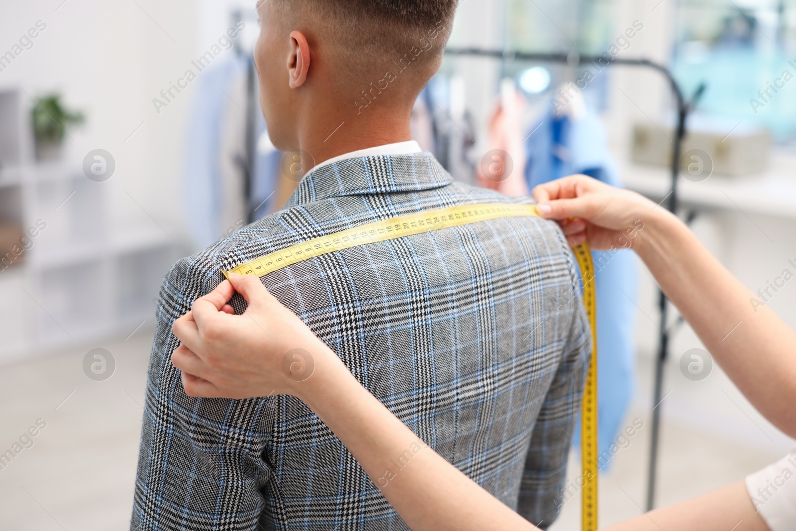 Photo of Tailor measuring jacket on man in atelier, closeup
