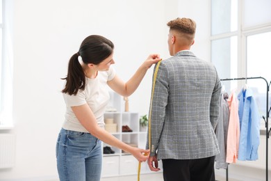 Photo of Tailor measuring jacket on man in atelier