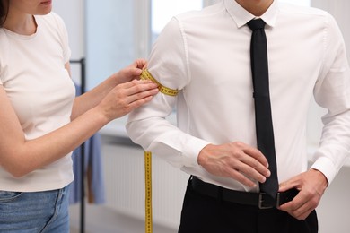 Photo of Tailor measuring man's arm in atelier, closeup
