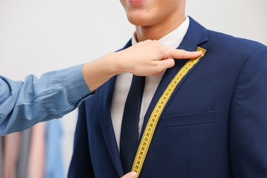 Photo of Tailor measuring jacket on man in atelier, closeup