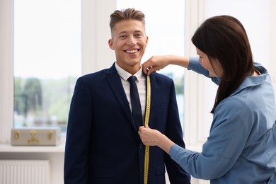 Photo of Tailor measuring jacket on man in atelier