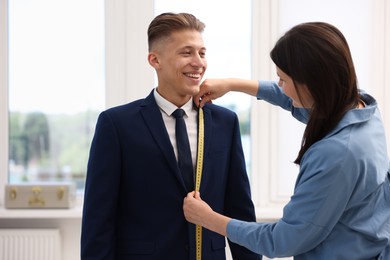 Photo of Tailor measuring jacket on man in atelier