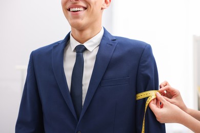 Photo of Tailor measuring jacket on man in atelier, closeup