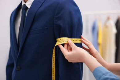Photo of Tailor measuring jacket on man in atelier, closeup