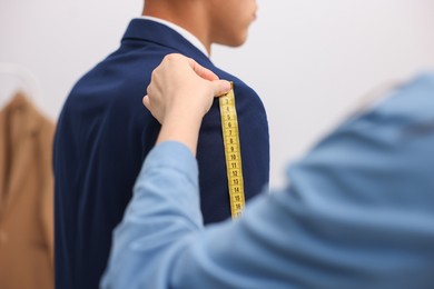 Photo of Tailor measuring jacket on man in atelier, closeup