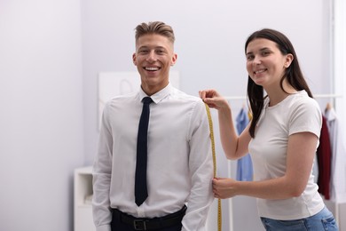 Photo of Tailor measuring woman's arm with tape in atelier