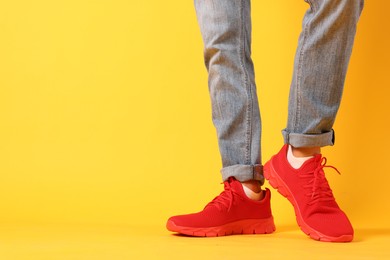 Photo of Man wearing pair of red sneakers on yellow background, closeup. Space for text