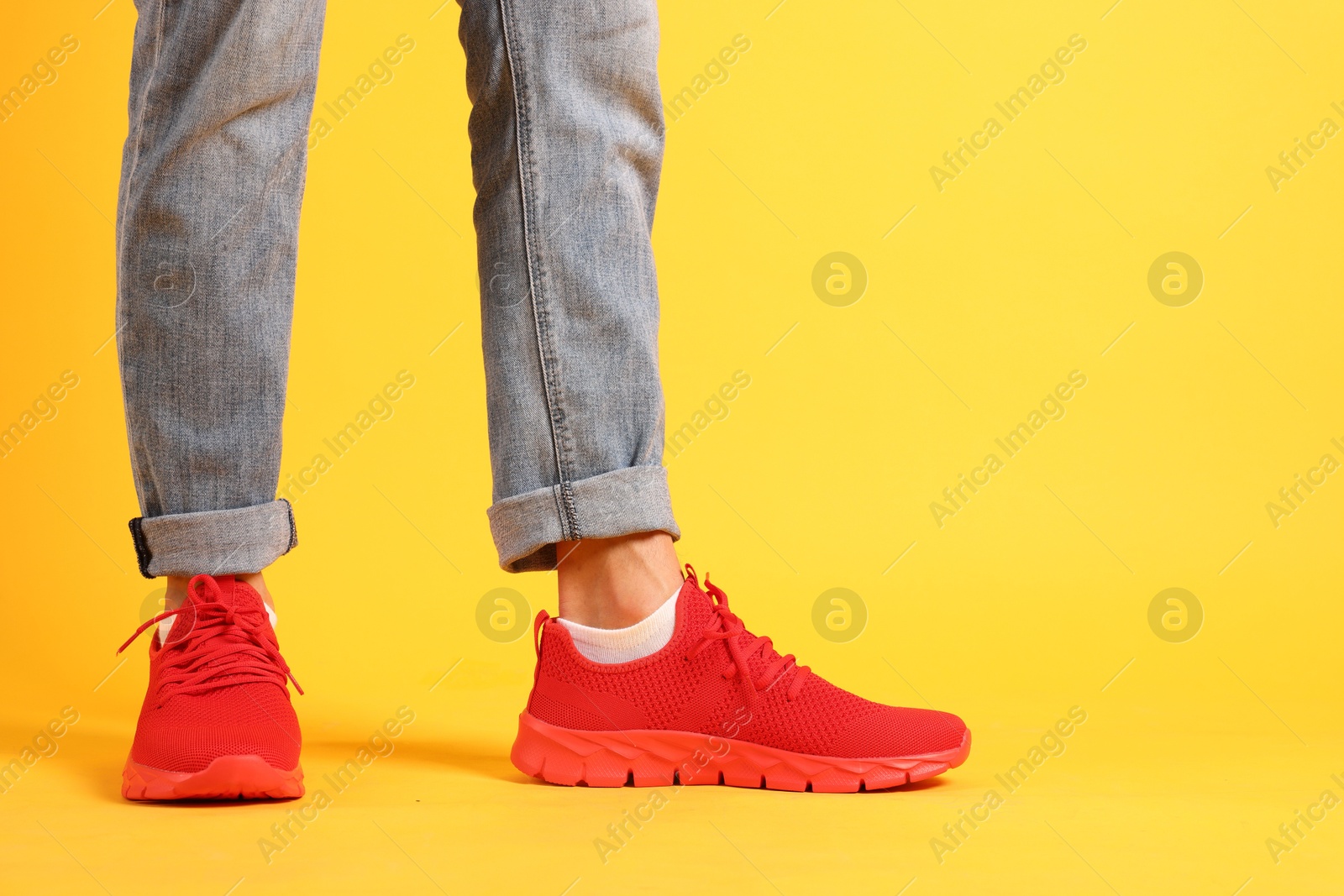Photo of Man wearing pair of red sneakers on yellow background, closeup. Space for text