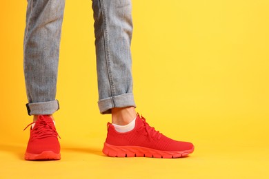 Photo of Man wearing pair of red sneakers on yellow background, closeup. Space for text