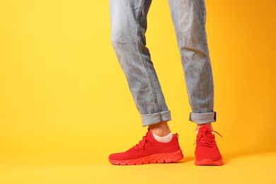 Photo of Man wearing pair of red sneakers on yellow background, closeup. Space for text