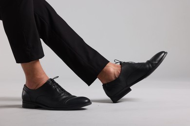 Photo of Man wearing pair of black leather shoes on light background, closeup