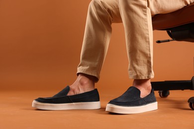 Photo of Man wearing pair of dark blue shoes on brown background, closeup