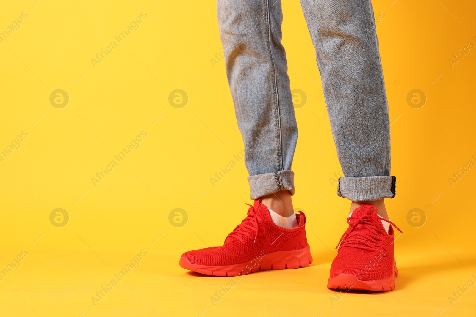 Photo of Man wearing pair of red sneakers on yellow background, closeup. Space for text
