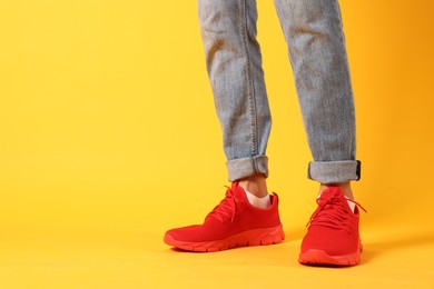 Photo of Man wearing pair of red sneakers on yellow background, closeup. Space for text