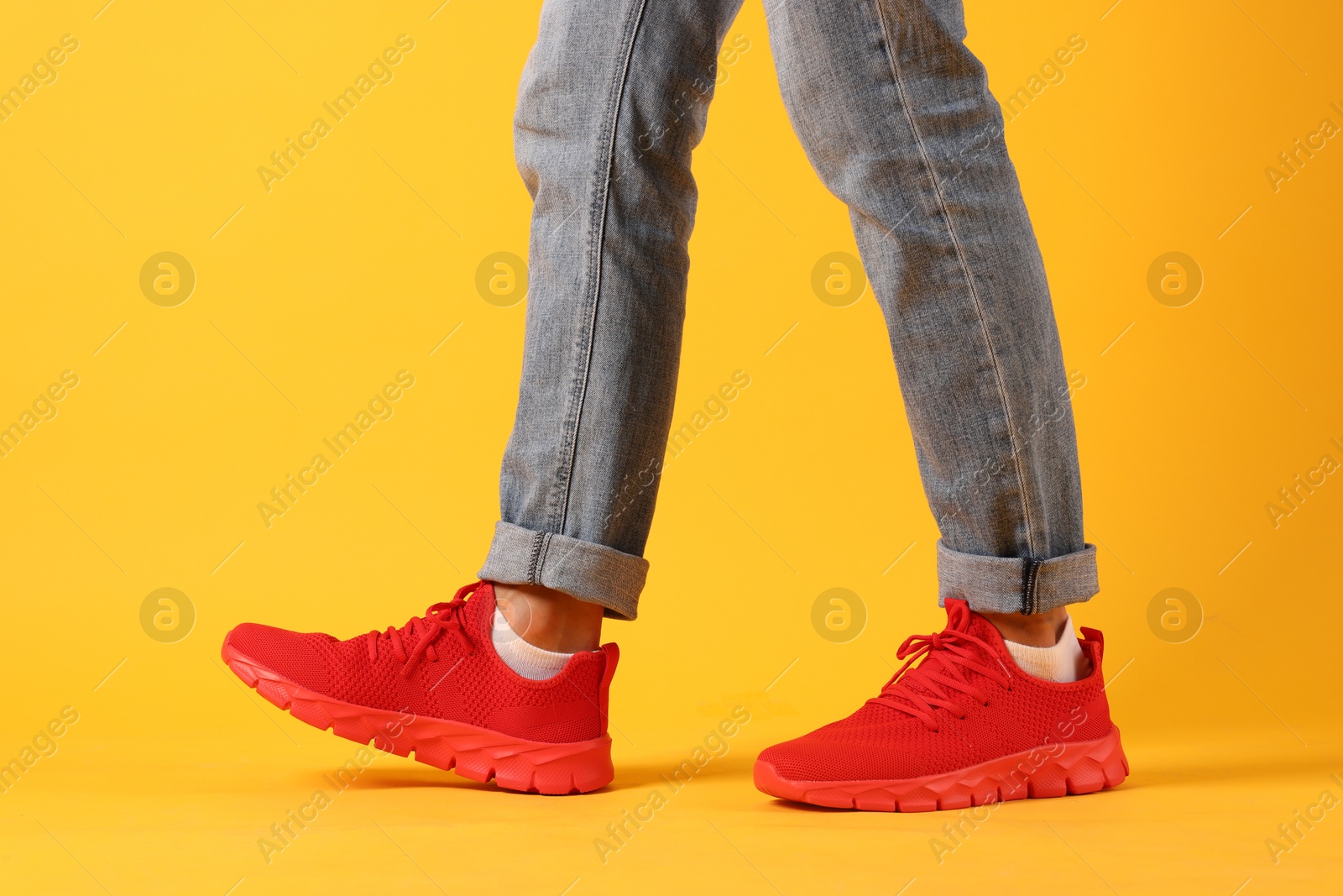 Photo of Man wearing pair of red sneakers on yellow background, closeup