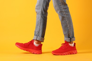Photo of Man wearing pair of red sneakers on yellow background, closeup
