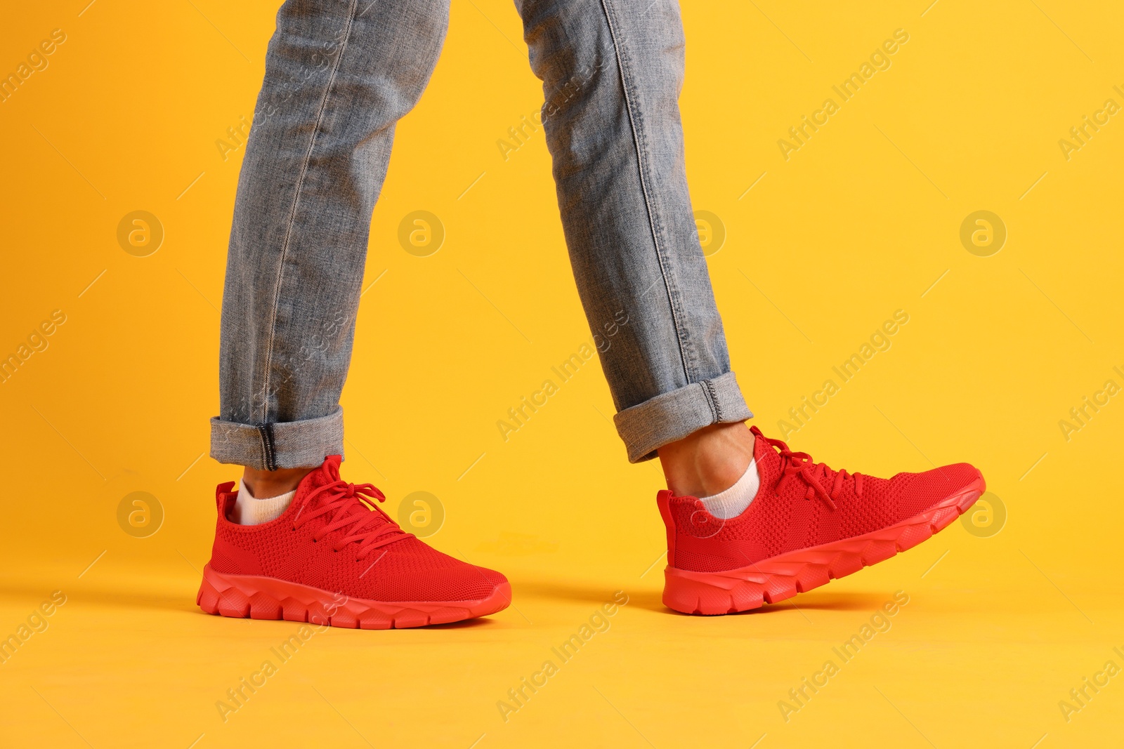 Man wearing pair of red sneakers on yellow background, closeup Photo of Man wearing pair of red sneakers on yellow background, closeup