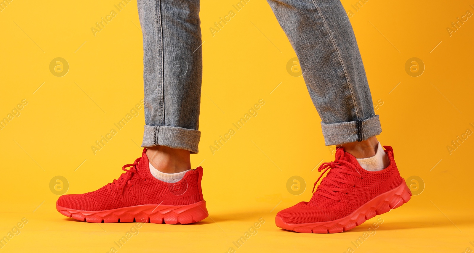 Photo of Man wearing pair of red sneakers on yellow background, closeup