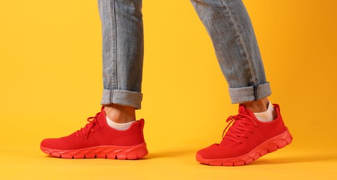 Photo of Man wearing pair of red sneakers on yellow background, closeup
