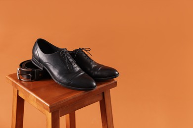 Photo of Pair of black leather shoes on stool against brown background. Space for text