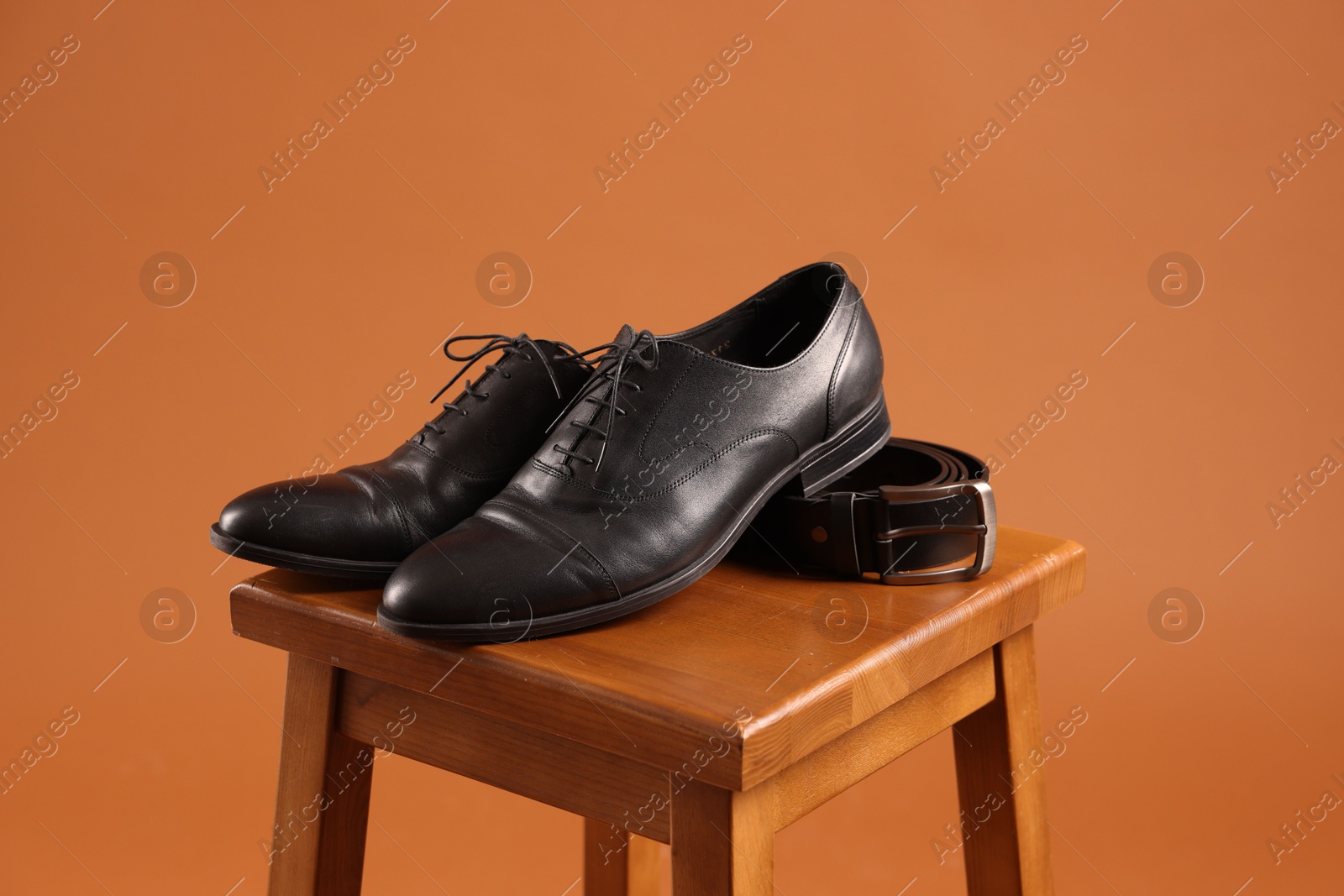 Photo of Pair of black leather shoes on stool against brown background