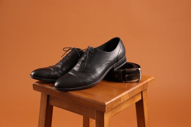 Photo of Pair of black leather shoes on stool against brown background