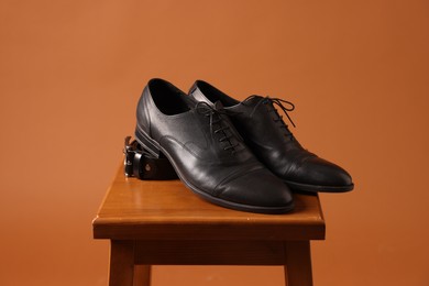 Photo of Pair of black leather shoes on stool against brown background