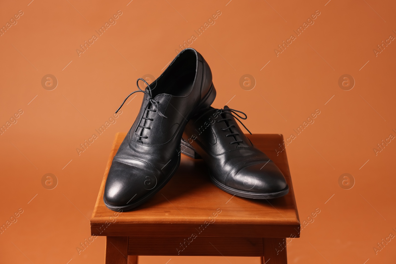 Photo of Pair of black leather shoes on stool against brown background