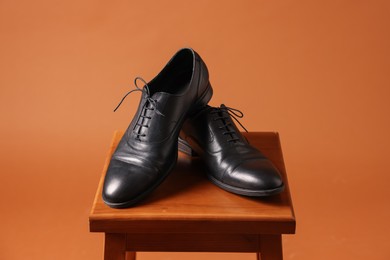 Photo of Pair of black leather shoes on stool against brown background
