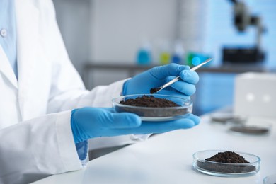 Photo of Scientist taking soil sample for research at white table in laboratory, closeup