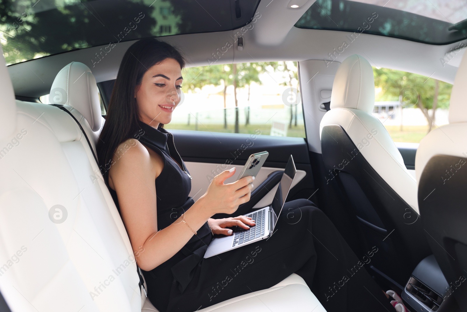 Photo of Woman with smartphone and laptop in modern car