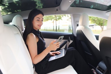 Photo of Woman with smartphone and laptop in modern car