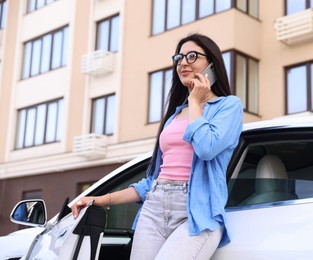 Photo of Woman talking on smartphone near car outdoors, low angle view