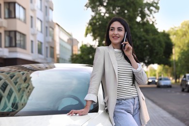 Photo of Beautiful woman talking on smartphone near car outdoors