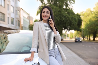 Photo of Beautiful woman talking on smartphone near car outdoors