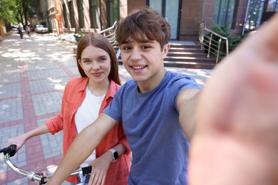 Photo of Teenage girl and boy with bicycle taking selfie on city street