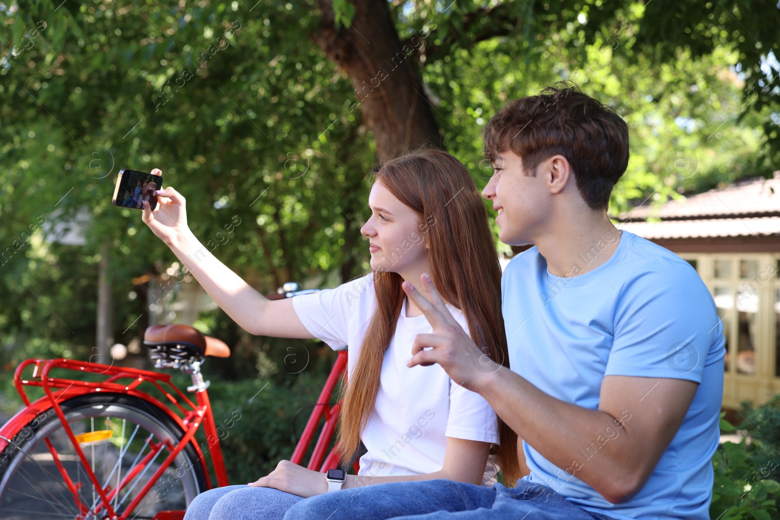 Photo of Teenage girl and boy with bicycles taking selfie on city street