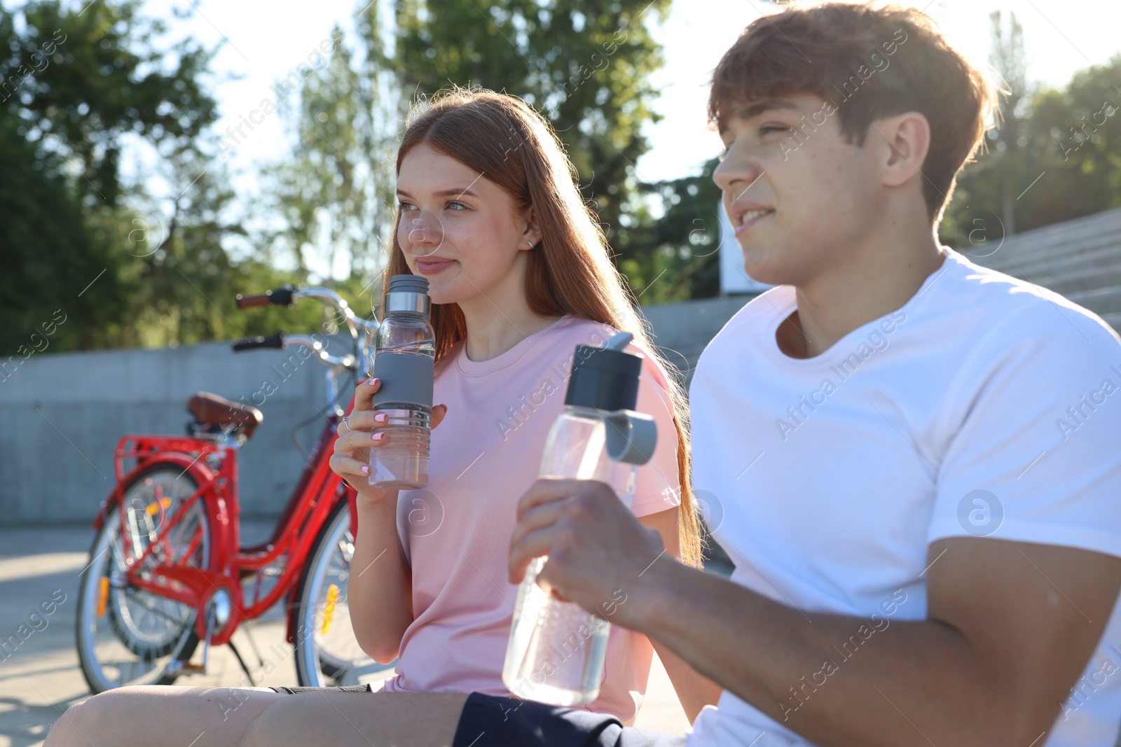 Photo of Teenage girl and boy drinking water near bicycle on city street