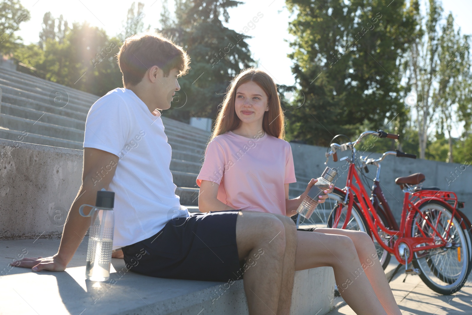 Teenage girl and boy sitting on stairs near bicycles on city street Photo of Teenage girl and boy sitting on stairs near bicycles on city street