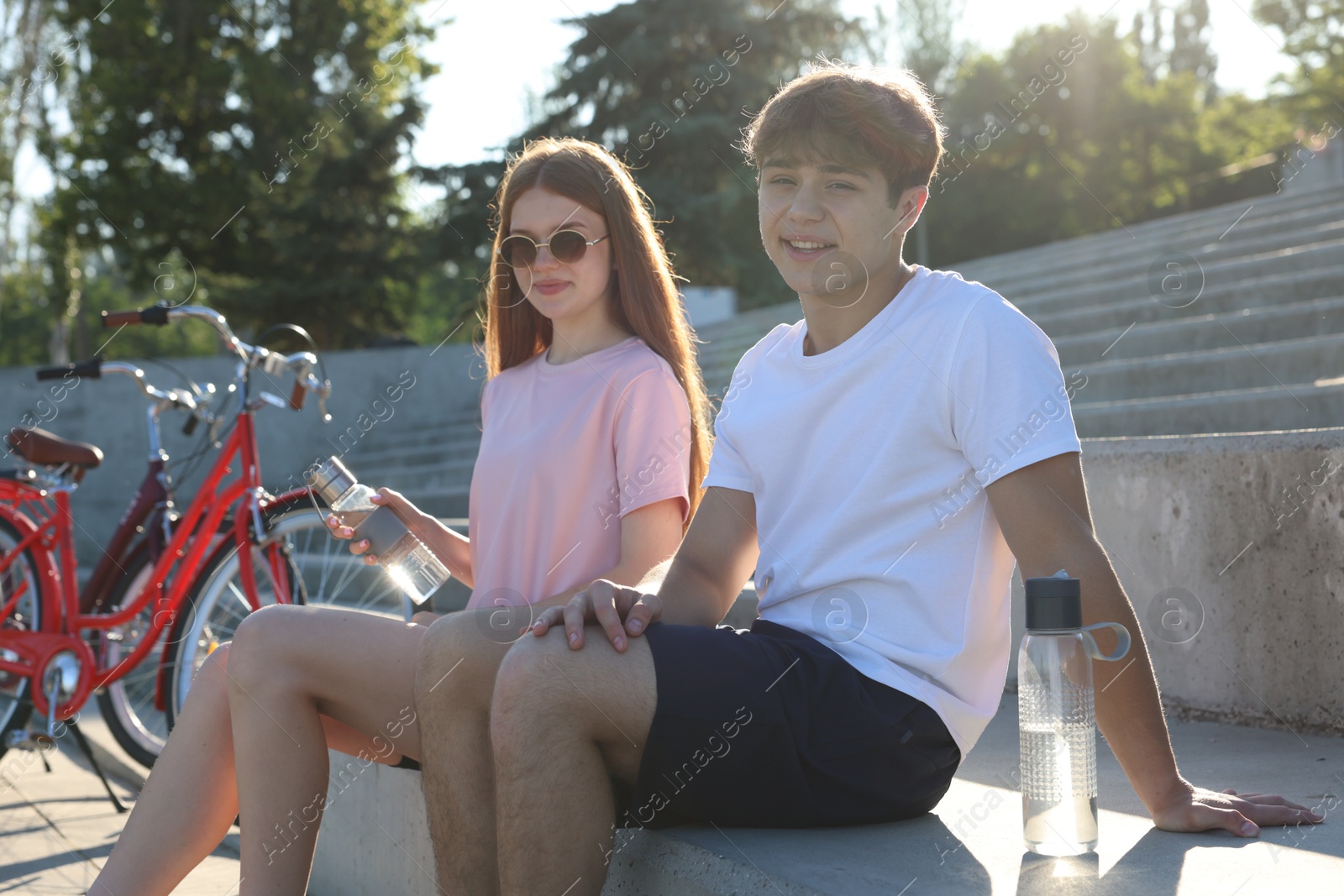 Teenage girl and boy sitting on stairs near bicycles on city street Photo of Teenage girl and boy sitting on stairs near bicycles on city street