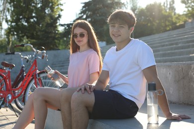Photo of Teenage girl and boy sitting on stairs near bicycles on city street